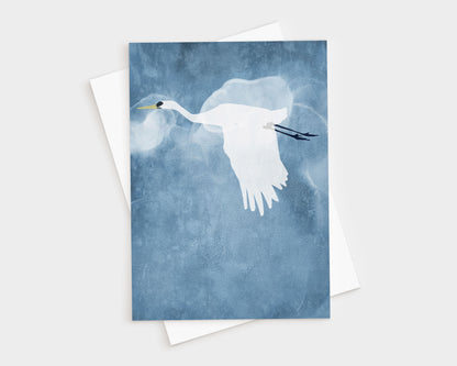 Minimalist illustration of a white heron flying against a moody blue background with subtle cloudy textures, wings partially down and legs trailing behind, with a white envelope peeking from behind the card.