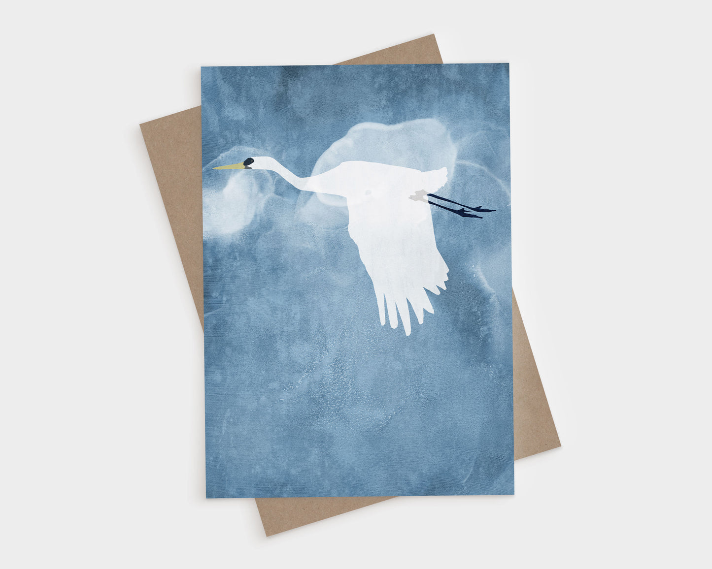 Minimalist illustration of a white heron flying against a moody blue background with subtle cloudy textures, wings partially down and legs trailing behind, with a kraft brown envelope peeking from behind the card.