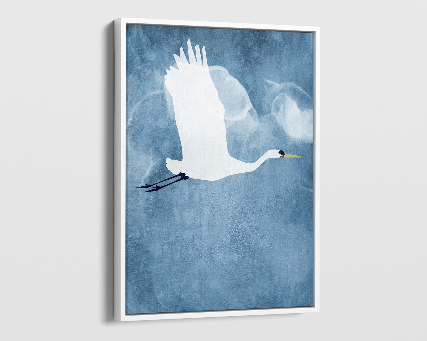 White framed canvas print of a white heron in mid-flight with wings raised, soaring against a textured blue sky with faint, cloud-like swirls.
