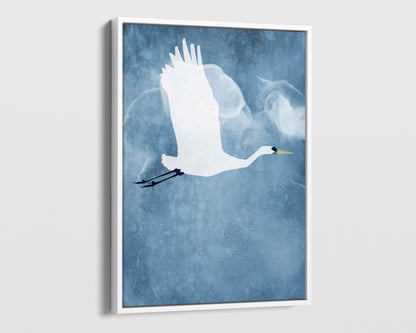White framed canvas print of a white heron in mid-flight with wings raised, soaring against a textured blue sky with faint, cloud-like swirls.