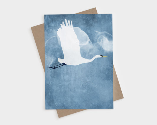 Greeting card featuring a white heron in flight with wings raised against a misty blue textured background, paired with a kraft brown envelope.