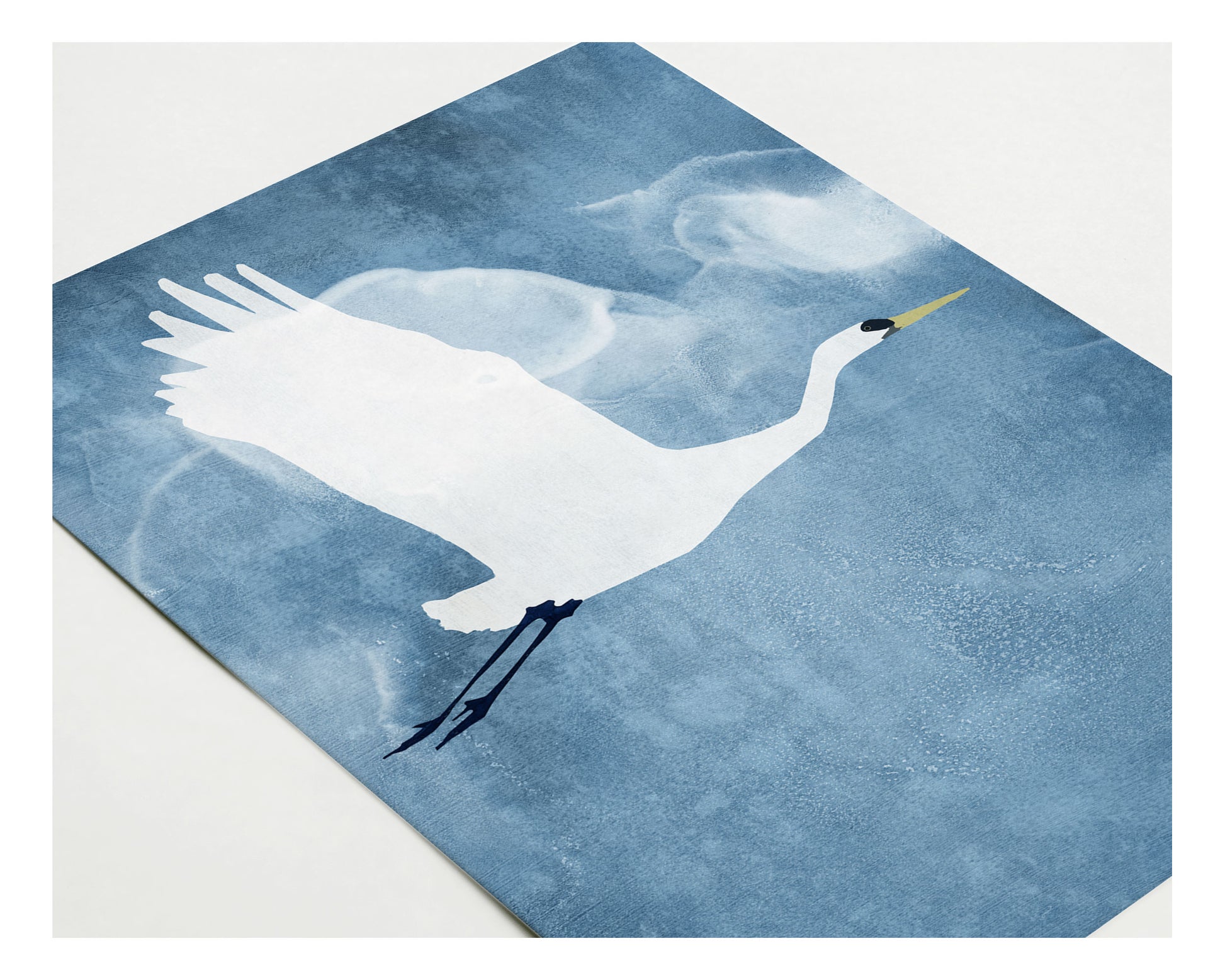 Close-up of a greeting card featuring a white heron with raised wings flying across a textured blue background, with soft, cloud-like shapes surrounding the bird.