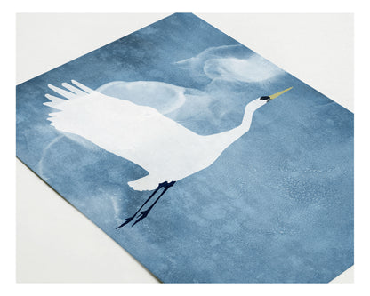 Close-up of a greeting card featuring a white heron with raised wings flying across a textured blue background, with soft, cloud-like shapes surrounding the bird.