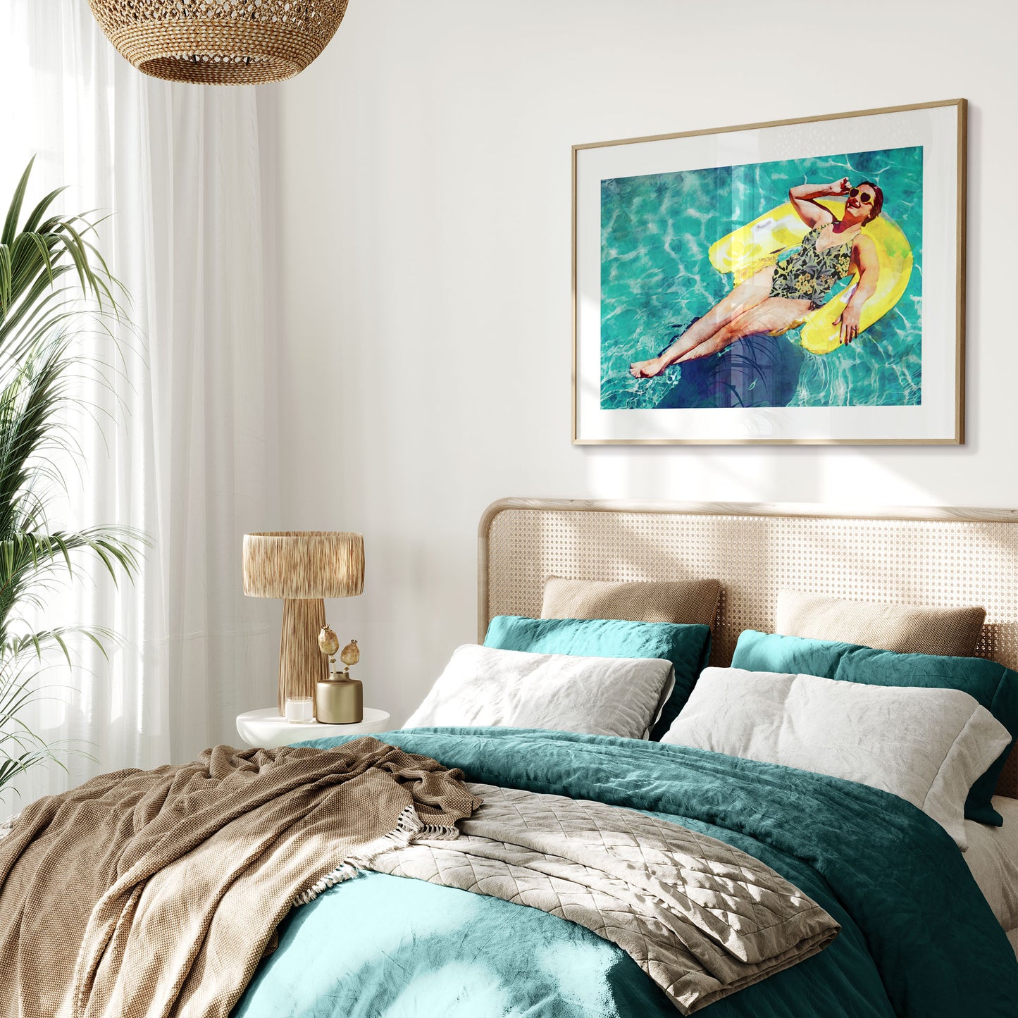 Bedroom with a woven headboard, teal and beige bedding, a side table with a lamp, and a framed picture of a woman on a yellow inflatable float hanging on the wall.