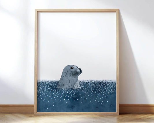 Minimalist art print of a gray spotted seal emerging from deep blue water, with its head and neck visible above the surface. The simple composition features a white background, textured rippling water, and soft shading, framed in light wood and displayed against a white wall.