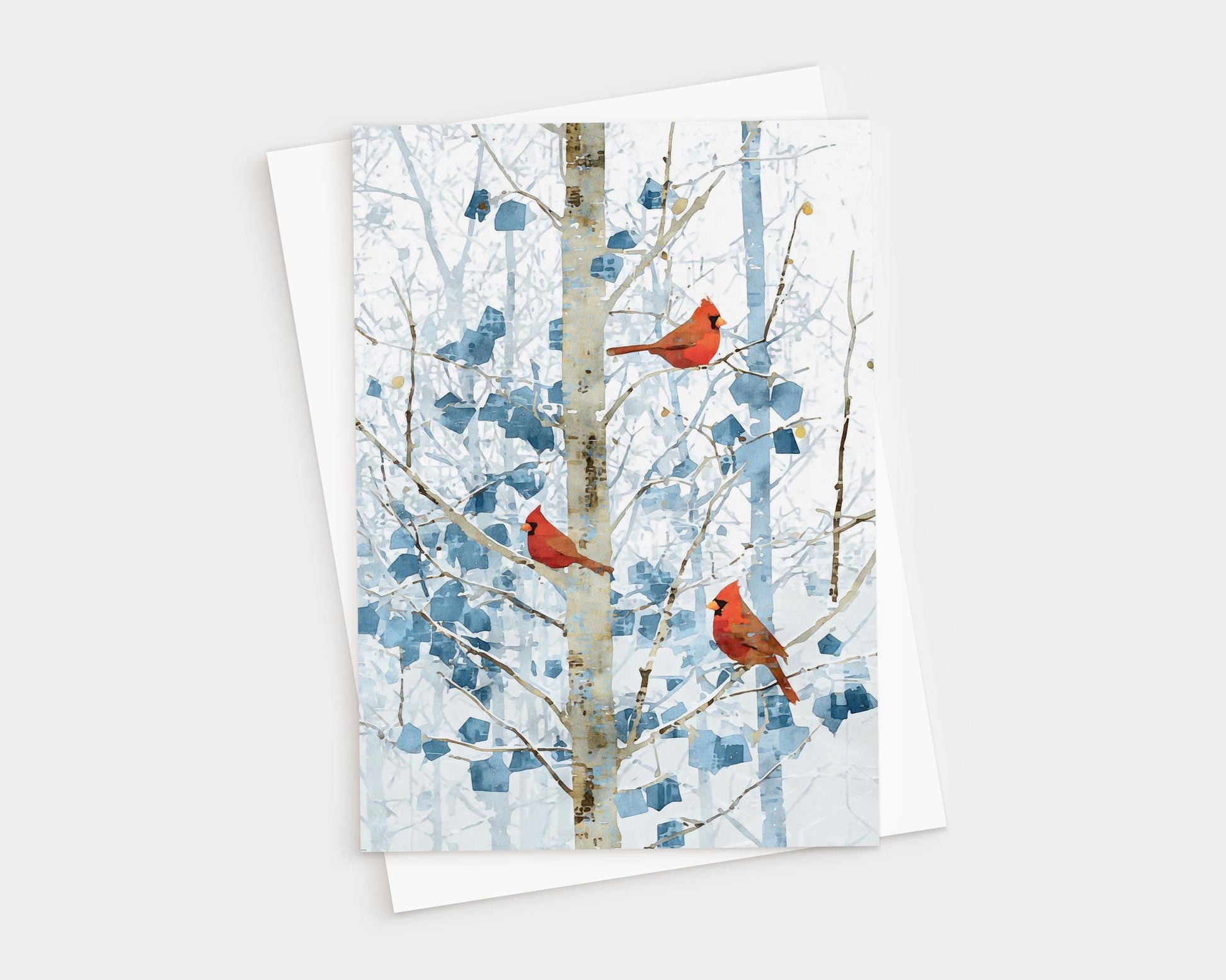 Greeting card featuring three bright red cardinals perched on slender branches of a winter tree. The background shows soft blue and white abstract foliage and a pale birch-like trunk, creating a serene snowy forest scene. Card is displayed on top of a white envelope against a light backdrop.