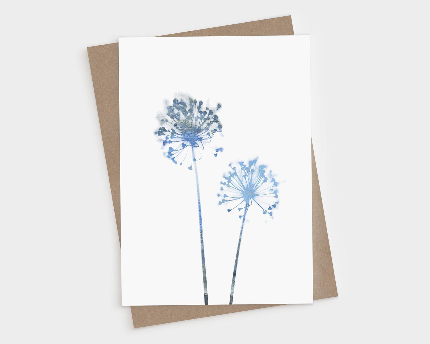 Minimalist greeting card featuring two delicate allium flower silhouettes in soft watercolor shades of blue, printed on white card stock. A kraft brown envelope is placed underneath.