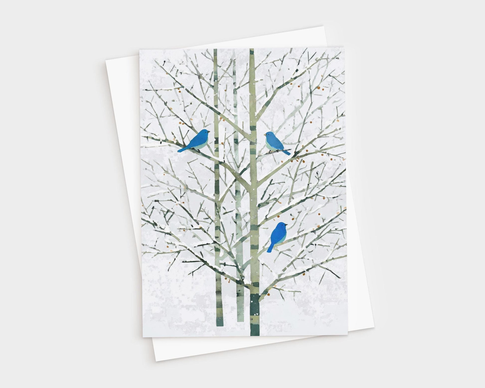 Greeting card featuring a minimalist watercolor-style illustration of three bright bluebirds perched on bare winter branches with pale green trunks and a soft white background. The card is shown with a white envelope, creating a natural, elegant presentation.