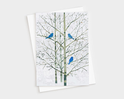 Greeting card featuring a minimalist watercolor-style illustration of three bright bluebirds perched on bare winter branches with pale green trunks and a soft white background. The card is shown with a white envelope, creating a natural, elegant presentation.