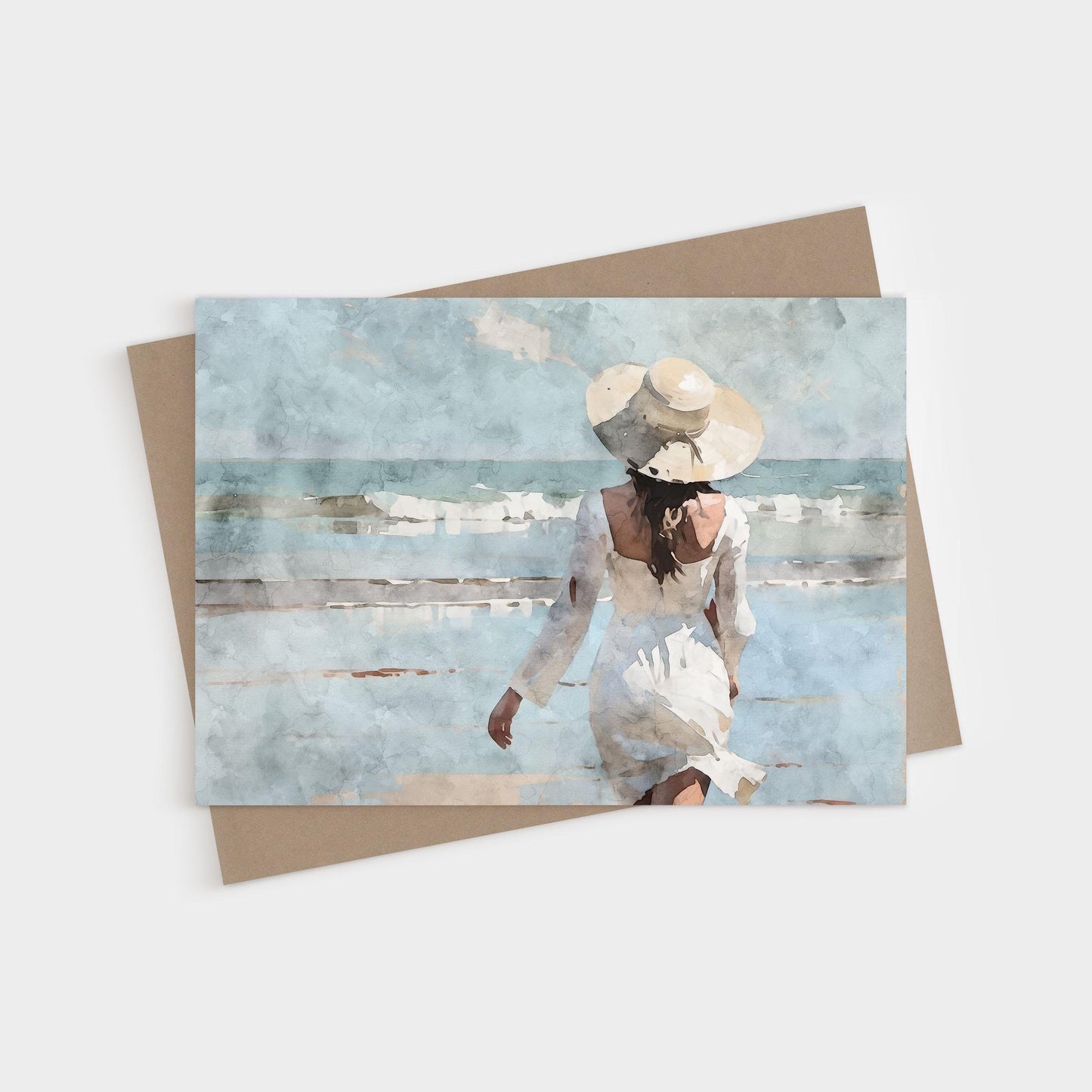 Watercolor-style greeting card showing a woman in a white dress and wide-brimmed hat walking toward ocean waves, paired with a kraft envelope on a light background.
