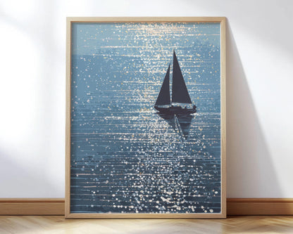 Framed art print featuring a stylized sailboat silhouette gliding across shimmering blue water, with sparkling light reflections rendered in a painterly, abstract dot pattern. The artwork is displayed in a natural wood frame and leaned against a white wall on a wood floor, creating a serene coastal vibe.
