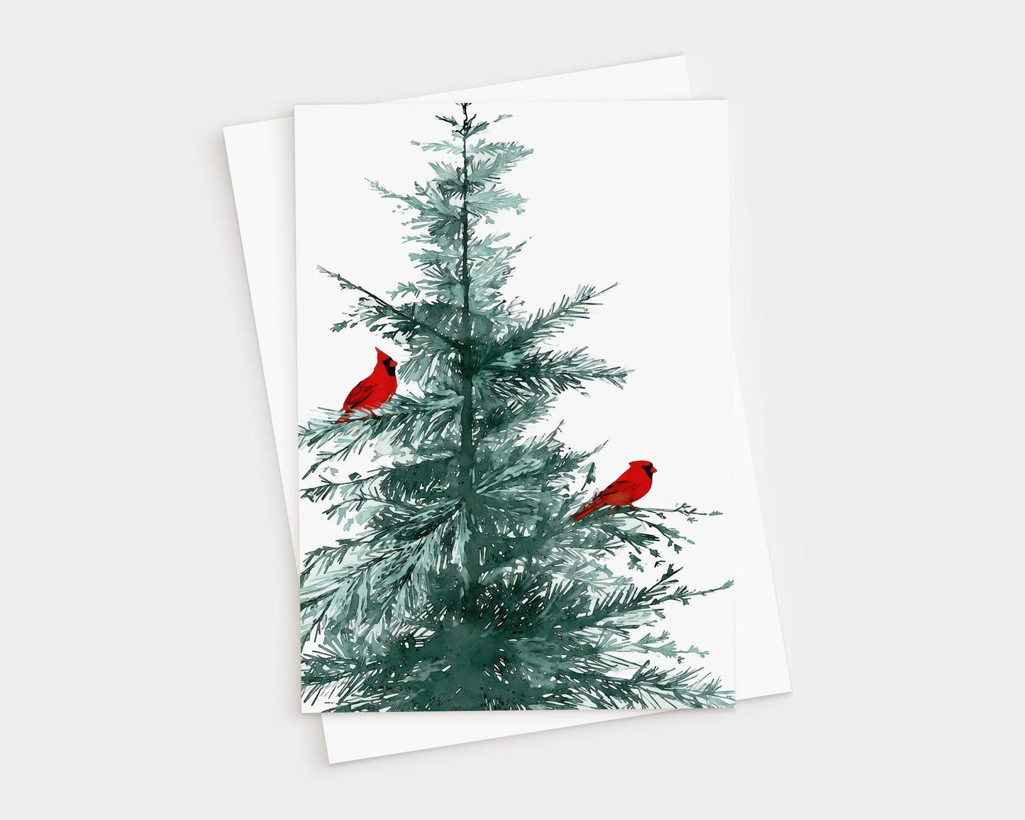 Greeting card featuring a watercolor illustration of a green pine tree with two bright red cardinals perched on its branches, displayed with a matching brown white envelope