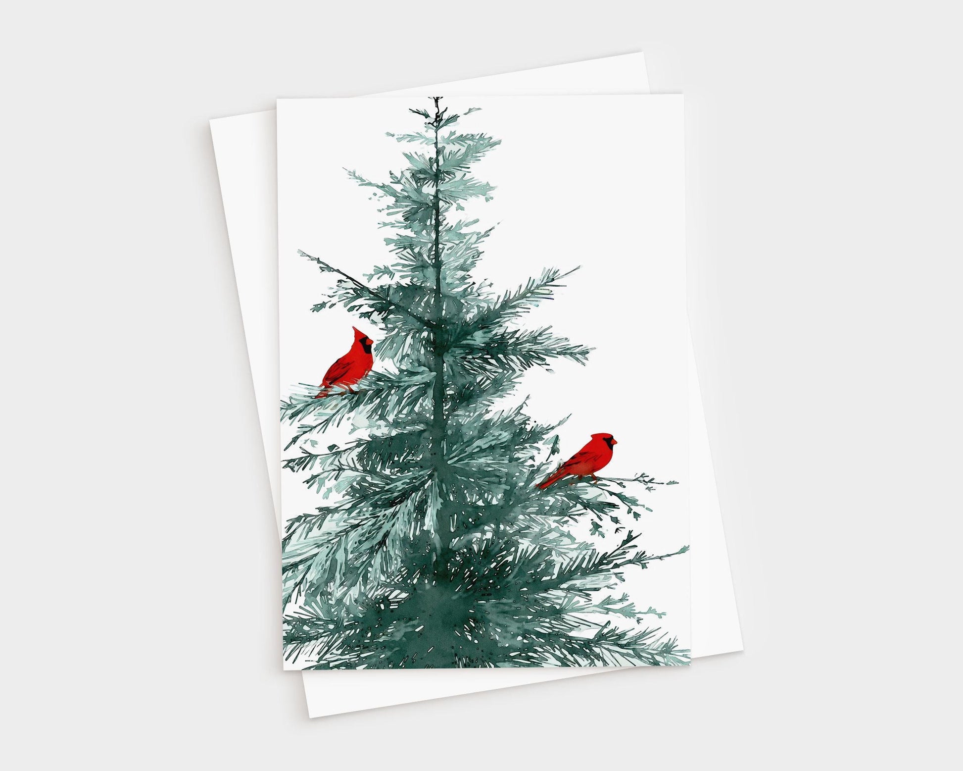 Greeting card featuring a watercolor illustration of a green pine tree with two bright red cardinals perched on its branches, displayed with a matching brown white envelope
