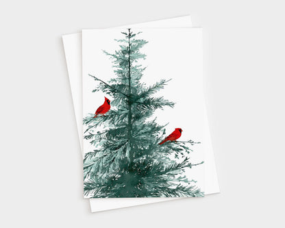 Greeting card featuring a watercolor illustration of a green pine tree with two bright red cardinals perched on its branches, displayed with a matching brown white envelope