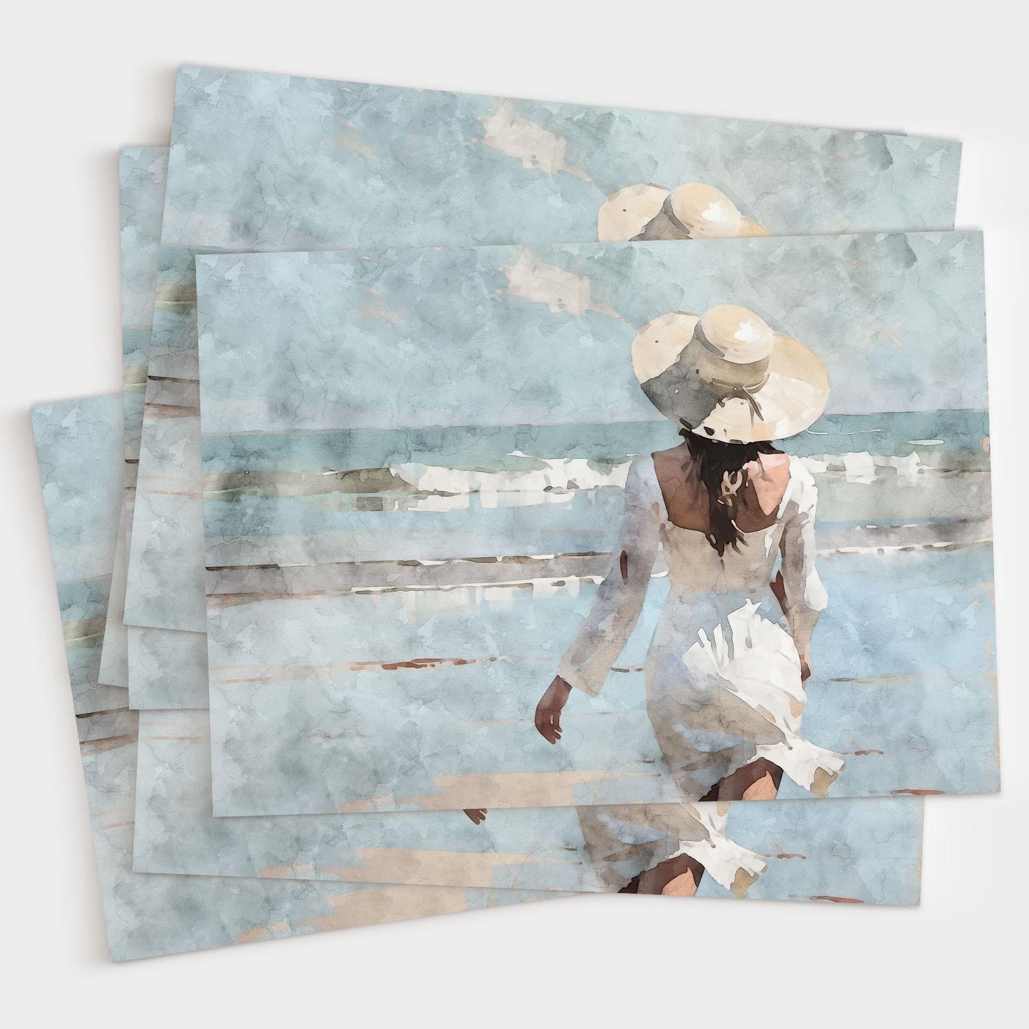 Stack of greeting cards featuring a watercolor-style painting of a woman in a flowing white dress and wide-brimmed hat walking toward gentle ocean waves under a soft blue sky.