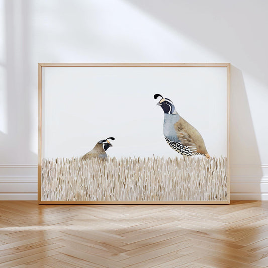 Minimalist watercolor art print of two California quail in tall beige grass, one standing and one crouched, with soft neutral tones and a light wood frame, displayed against a white wall on a herringbone wood floor.