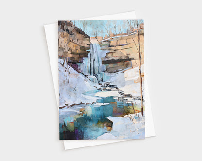 Watercolor-style greeting card featuring a winter waterfall cascading down rocky cliffs into a partially frozen pool. Snow blankets the ground and ice edges the turquoise-blue water, with bare trees silhouetted against a pale sky. A natural, serene winter landscape.
