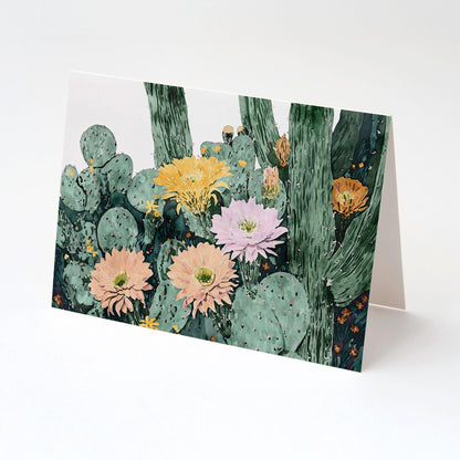 Folded greeting card with watercolor cactus illustration, showing clusters of green pads and tall stems with blooming flowers in peach, pink, yellow, and orange tones, displayed on a clean white background.