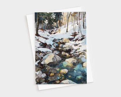 Watercolor-style greeting card featuring a rocky creek running through a snowy forest. Sunlight filters through bare trees, reflecting on the icy water in shades of blue and green. The card is displayed with a white envelope.