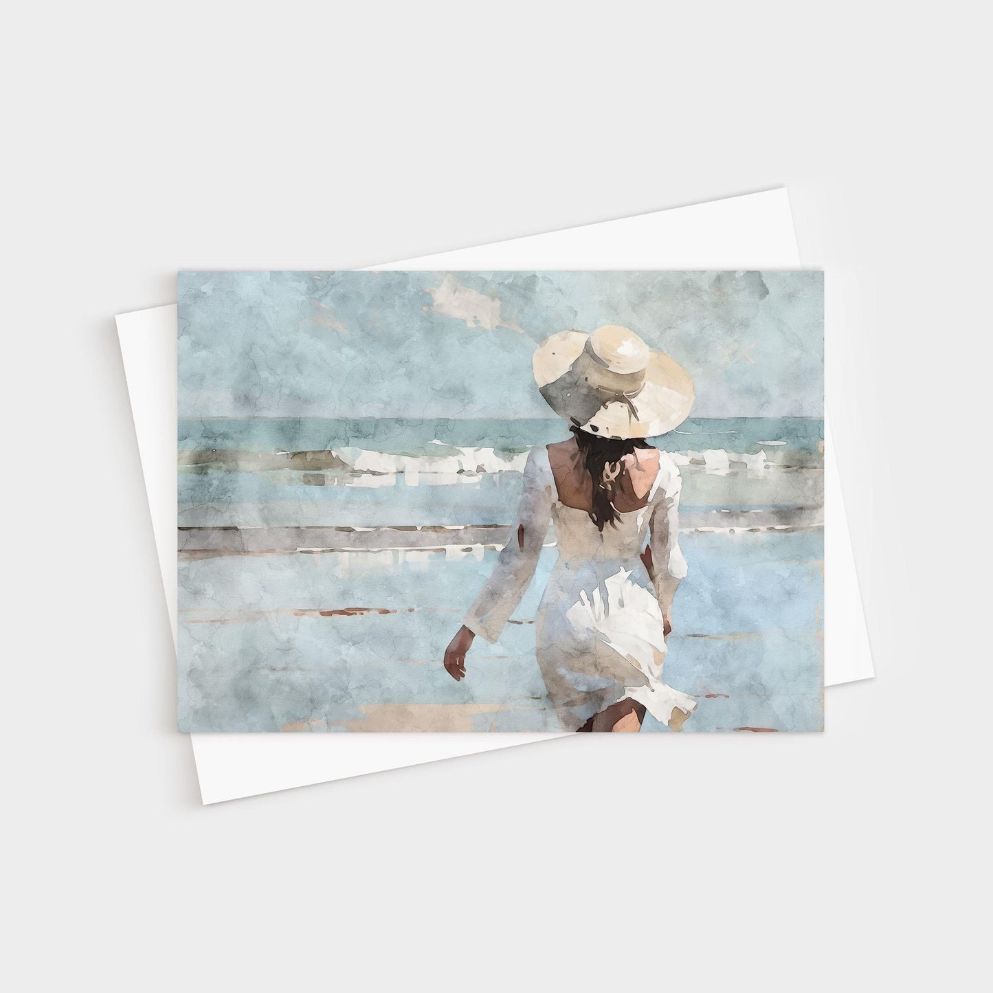 Greeting card featuring a watercolor-style painting of a woman in a flowing white dress and wide-brimmed hat walking toward gentle ocean waves under a soft blue sky.