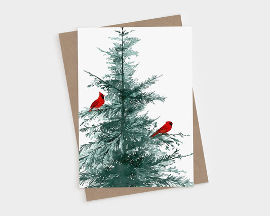 Greeting card featuring a watercolor illustration of a green pine tree with two bright red cardinals perched on its branches, displayed with a matching brown kraft envelope on a white background.