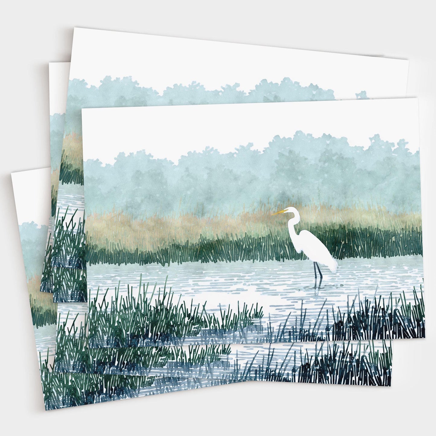 Set of greeting cards featuring a watercolor-style illustration of a white heron standing in a marsh with tall grasses, calm rippling water, and misty blue-green trees in the background. Cards are shown slightly fanned out in a stack.