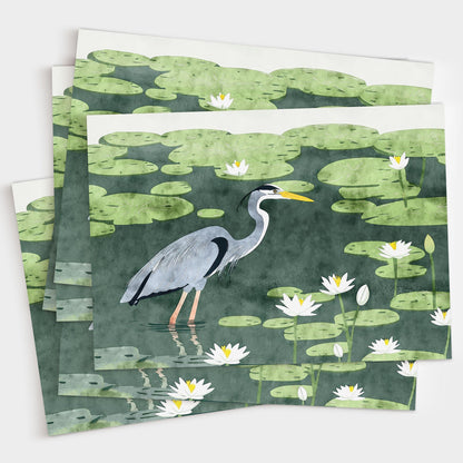 Stack of greeting cards featuring an illustration of a great blue heron standing in a pond filled with lily pads and white water lilies. The cards are slightly fanned out on a white background, showcasing the consistent, vibrant nature-themed design.