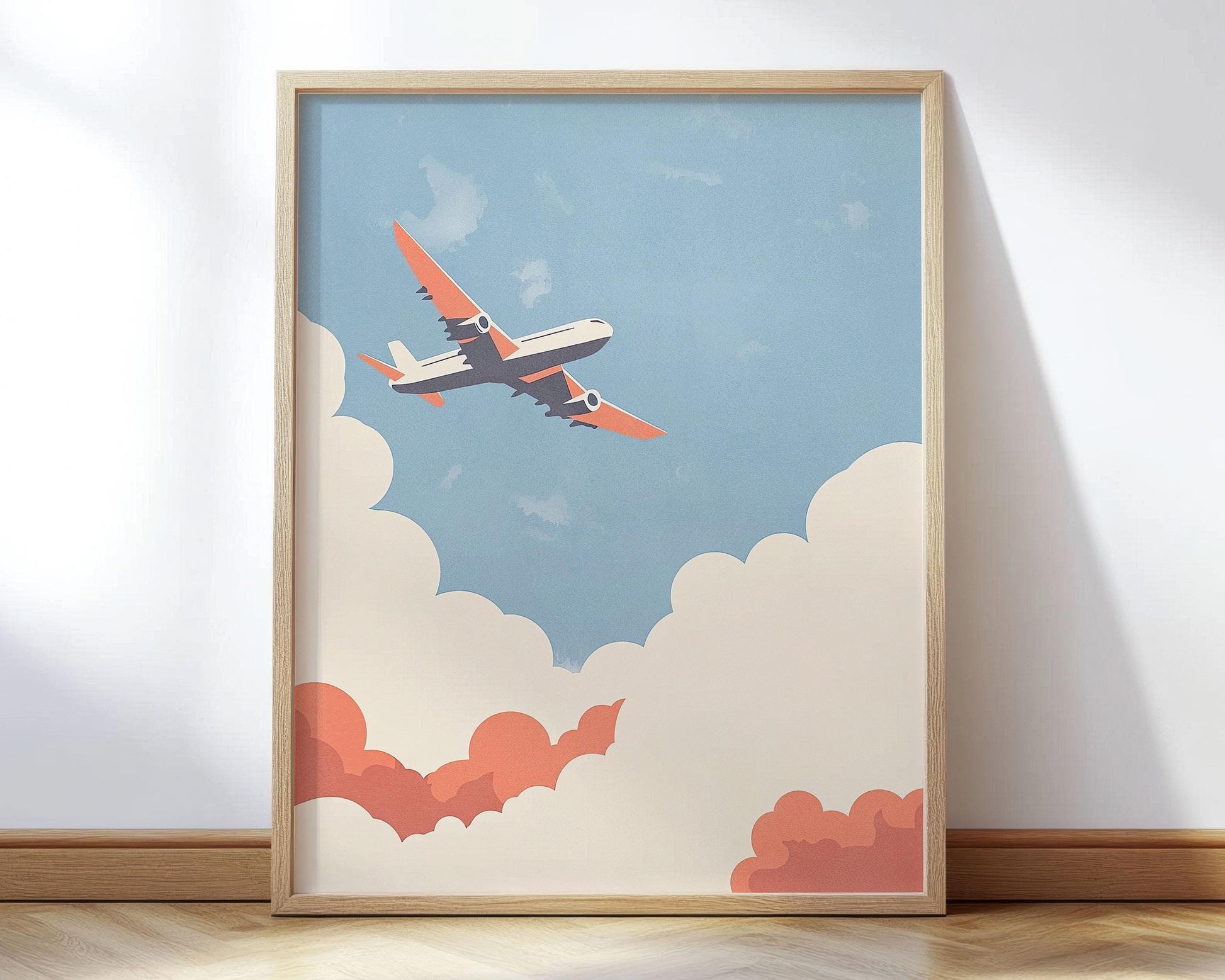 Framed art print featuring a stylized illustration of an airplane with orange wings flying upward through cream and coral clouds against a soft blue sky; displayed leaning against a white wall on a light wood floor.