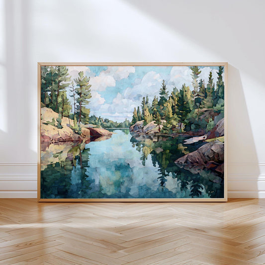 Framed landscape painting of a calm northern Minnesota lake, with evergreen trees and rocky shorelines reflected in the still blue-green water under a partly cloudy sky. The artwork uses soft, impressionistic brushstrokes in greens, blues, and earthy tones, leaning against a white wall on a wooden floor.