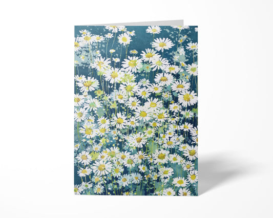 Greeting card standing upright featuring a watercolor-style field of white daisies with yellow centers on a deep blue-green background, creating a bright, fresh floral design against a clean white backdrop.
