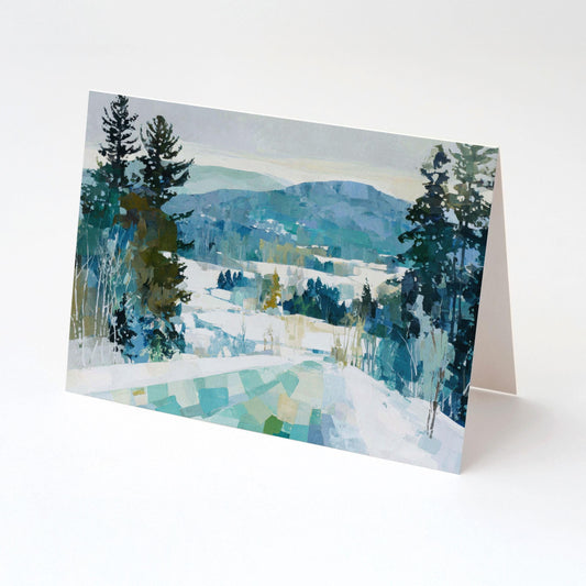 Folded greeting card featuring a winter mountain landscape painting with snow-covered hills, tall evergreen trees, and layered blue-green mountains in the distance.