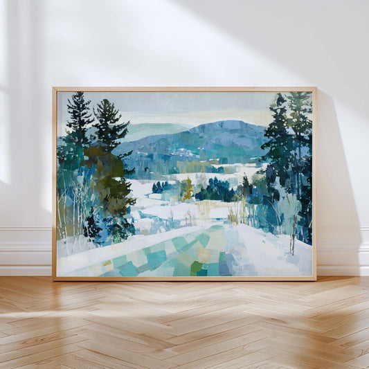 Framed painting of a winter mountain landscape, featuring snow-covered hills, evergreen trees, and layered blue and green tones, leaning against a white wall on a wooden herringbone floor with natural light casting shadows.