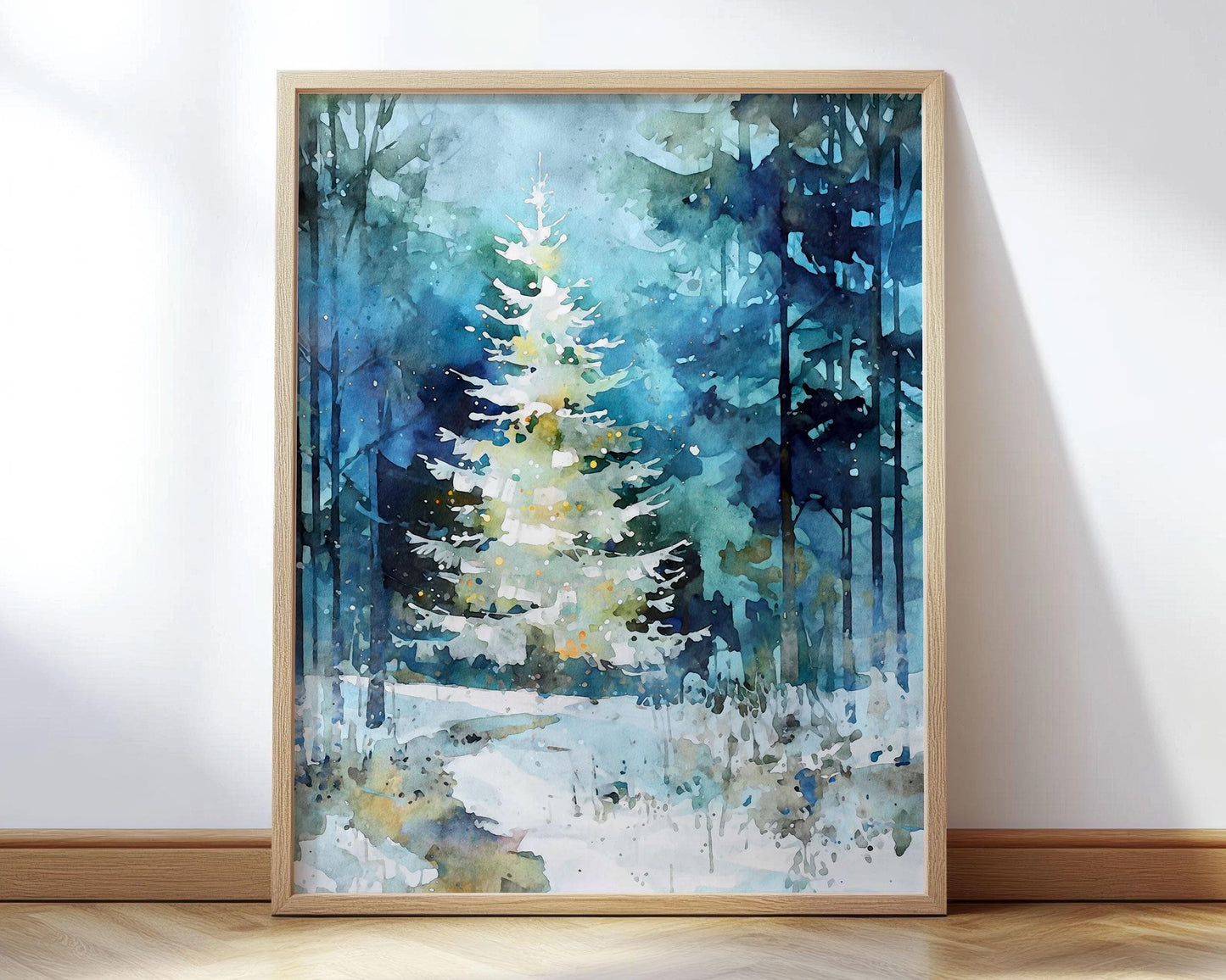 A watercolor-style painting of a glowing white Christmas tree in a snowy forest, framed in light wood and leaning against a wall. Deep blues and greens create a wintry backdrop with tall trees, soft snow, and scattered light speckles that give the scene a peaceful, magical feel.
