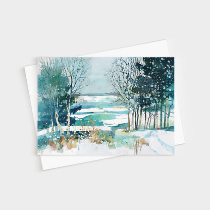 Watercolor greeting card featuring a serene winter landscape with snow-covered fields, bare trees, and evergreens in shades of blue, teal, and white, with soft brushstrokes and splattered paint suggesting falling snow. Card is displayed with a white envelope.