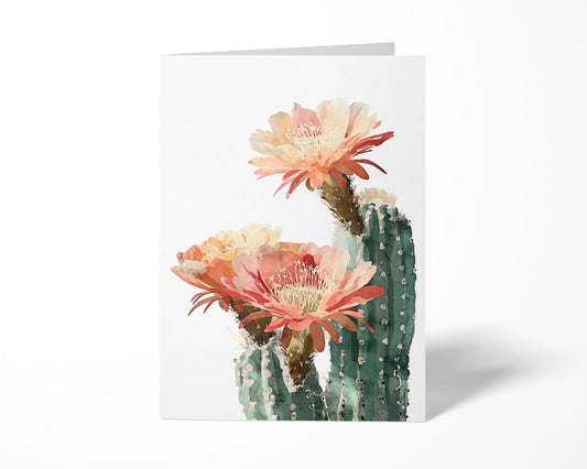 Standing greeting card with watercolor illustration of a green cactus topped with three large coral, peach, and cream blossoms, displayed against a clean white background.
