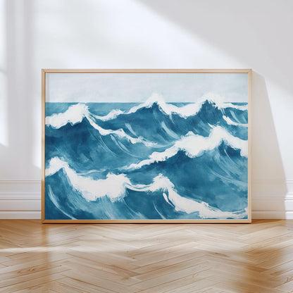 Large framed ocean wave painting leaning against a white wall on a wood herringbone floor. The artwork features bold, painterly blue waves with frothy white crests, capturing the movement and energy of the sea in a serene, contemporary style.