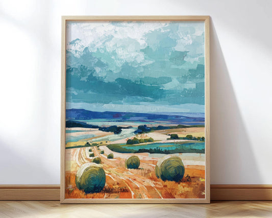 Framed impressionist-style painting of a countryside landscape featuring golden fields with round hay bales in the foreground, winding paths, distant blue hills, and a dramatic sky in shades of turquoise and teal.