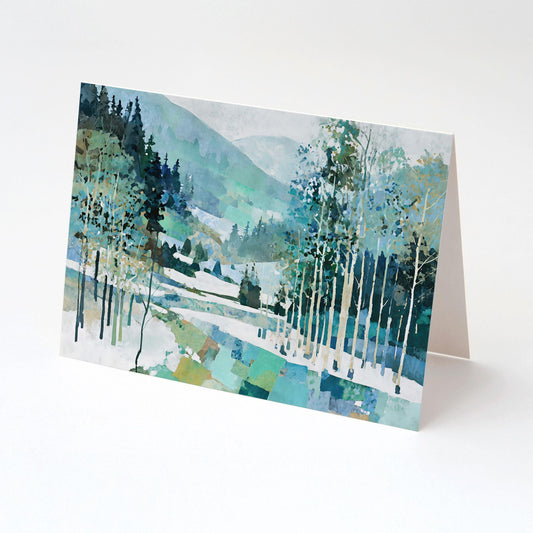 Folded greeting card displayed upright, featuring a watercolor-style winter forest scene with birch trees, evergreens, and snow-covered hills in cool tones of blue, green, and white, evoking a serene mountain landscape.