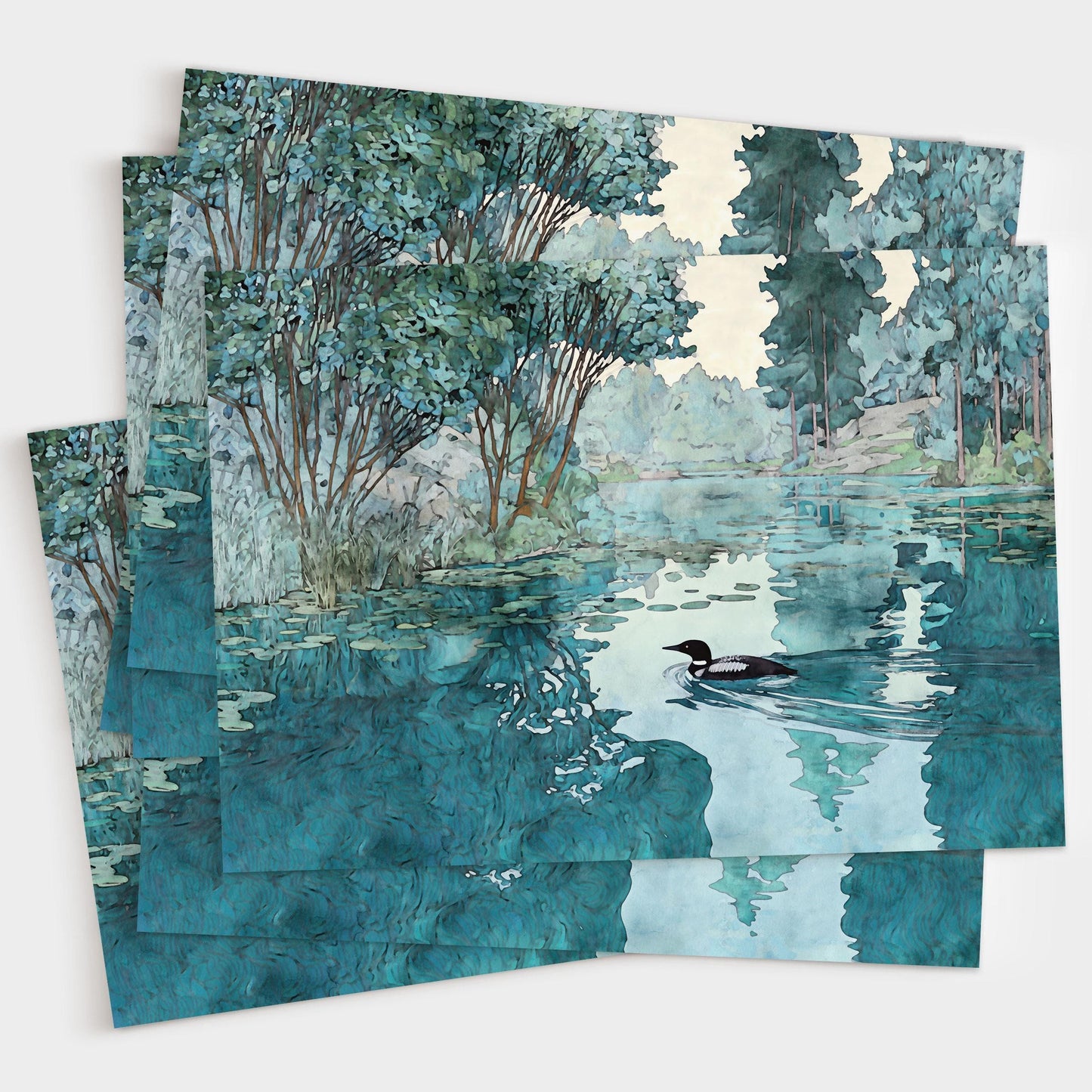 Set of greeting cards featuring a watercolor-style illustration of a loon gliding across a calm lake surrounded by trees. The overlapping cards display rich teal and green tones with soft reflections in the water, creating a serene, nature-inspired design.