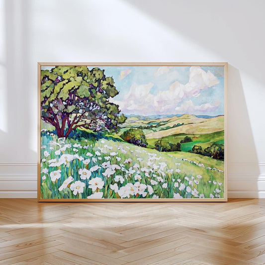 Framed painting of a sunlit meadow filled with white wildflowers and a large tree on the left, overlooking rolling green hills under a bright blue sky with fluffy white clouds.
