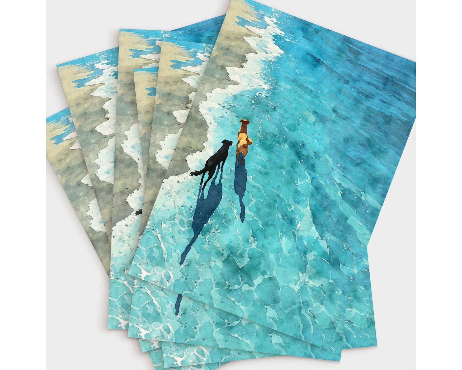 Set of greeting cards fanned out on a white surface, each featuring a watercolor-style illustration of two dogs walking along the shoreline. The vivid turquoise water and foamy waves create a sunlit, serene beach scene, with long shadows trailing behind the dogs.